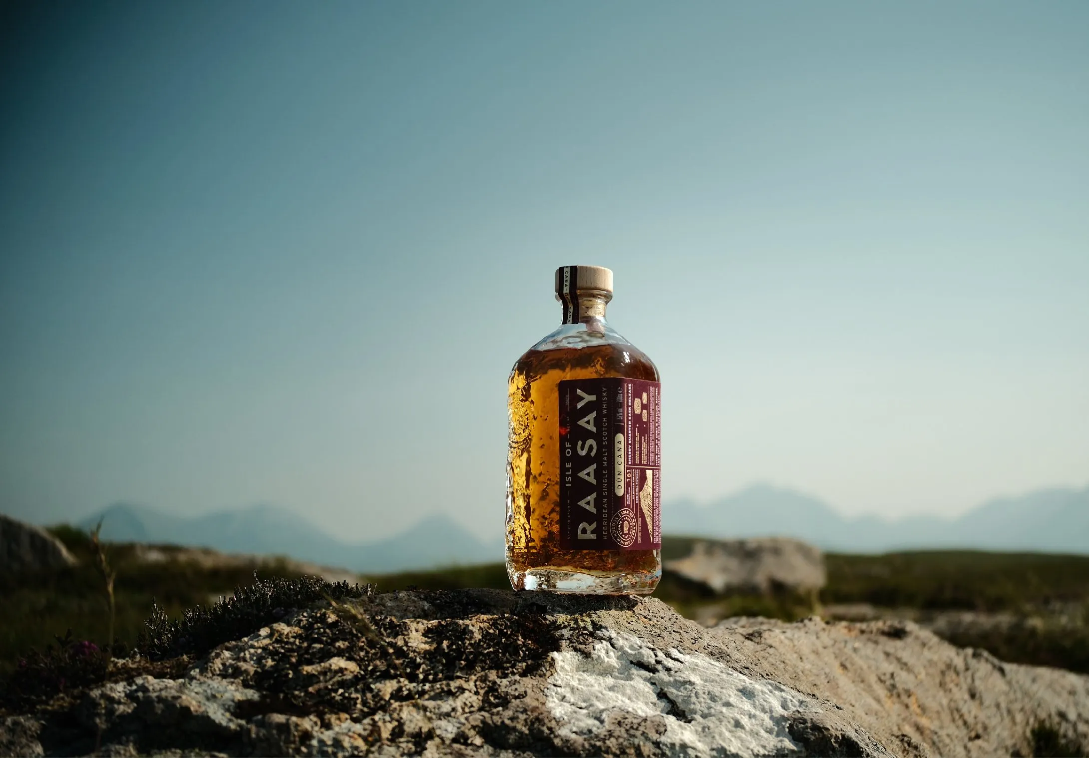A bottle of Isle of Raasay The Draam on a rocky outcrop above the sea, with the hills of Skye beyond